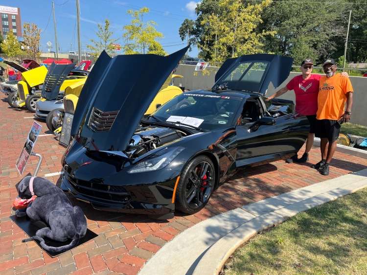 Two men standing beside a C7 Corvette coupe.