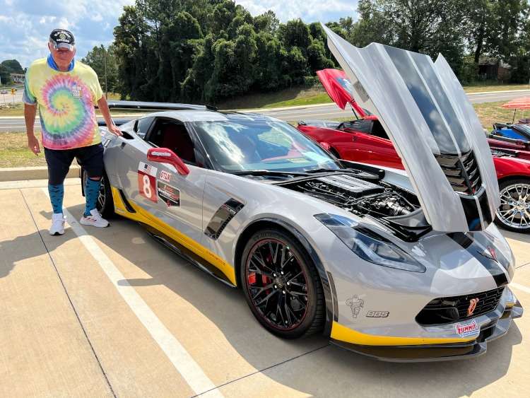 A man standing beside a gray C7 Corvette coupe.