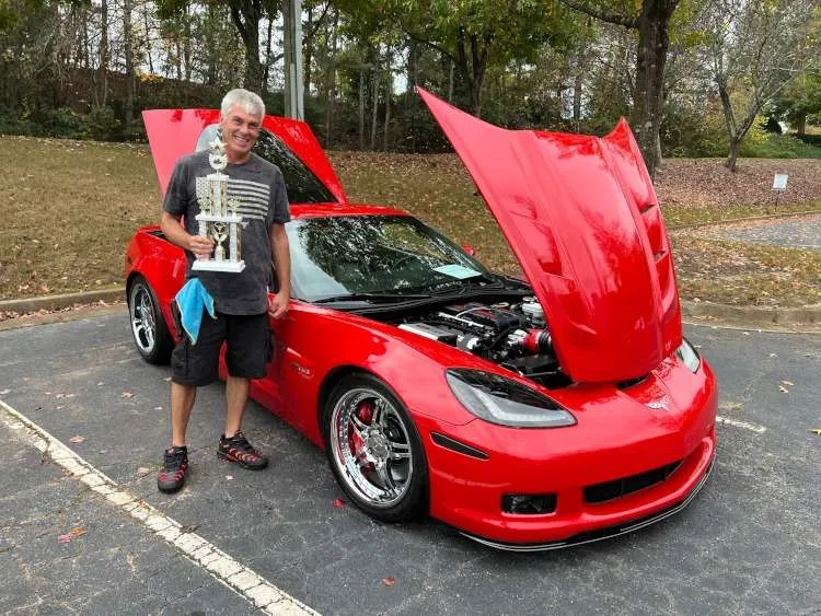A man holding a trophy beside a red Corvette.
