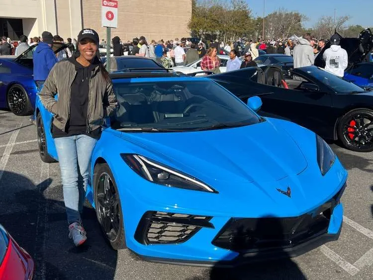 A woman is standing beside a C8 Corvette