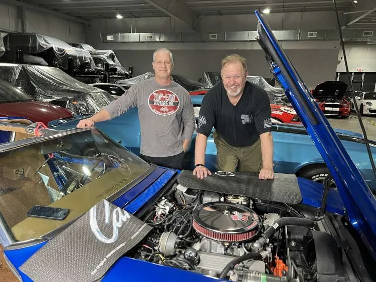 Two men beside a blue Corvette