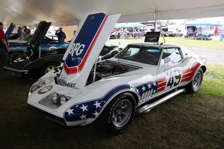 A white 1968-1972 C3 Corvette race car with blue and red stars and stripes livery, a large number '49', and its hood open on display at Corvettes at Carlisle 2025. Photo from Vettes of Atlanta Magazine.