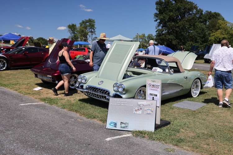 A light green 1959 Chevrolet Corvette 'Roadster Restomod' with its hood open on display at the Corvettes at Carlisle 2025 event, alongside other classic and modern Corvettes. Photo from Vettes of Atlanta Magazine.