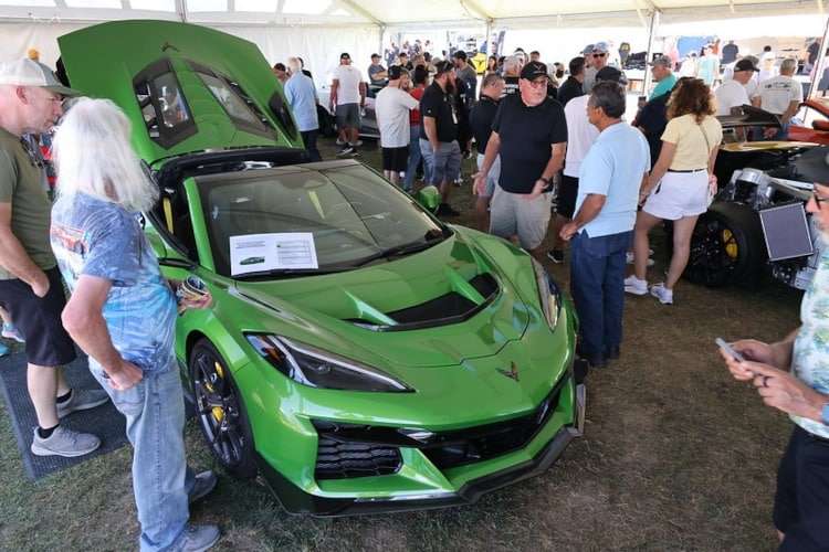A bright green C8 Corvette Z06 with its hood and engine cover open, surrounded by a crowd of people at the Corvettes at Carlisle 2025 event.