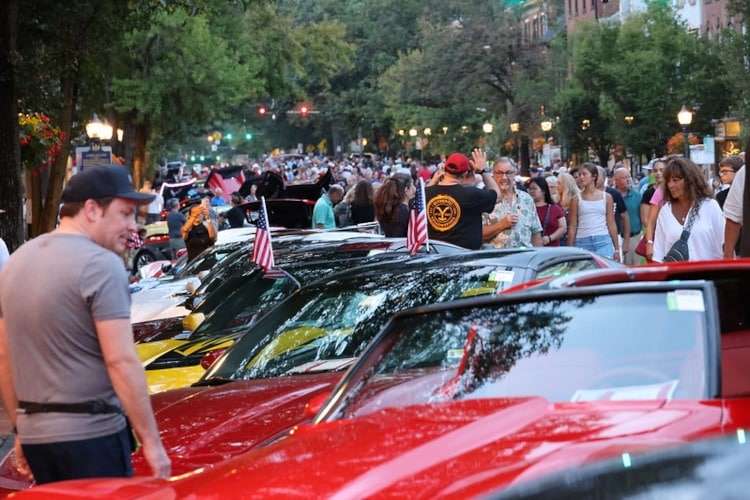 Row of colorful Corvettes, including a red C7, parked in Downtown Carlisle with spectators and drivers mingling during the annual Corvettes at Carlisle event. Photo from Vettes of Atlanta Magazine.