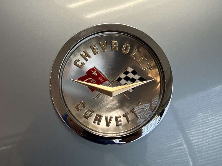 Close-up of a perfectly preserved chrome "Chevrolet Corvette" emblem on a 1958 model, featuring the iconic crossed flags and a classic v-shape.