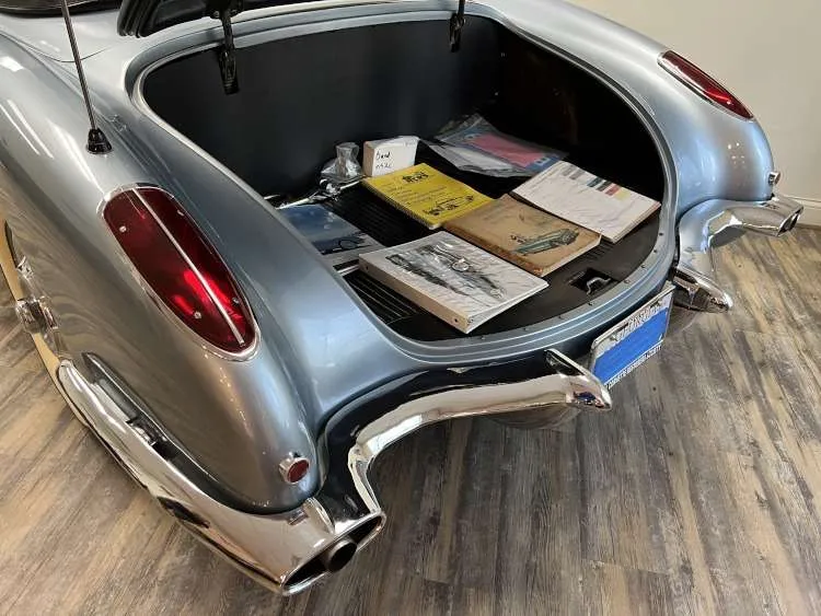 The open trunk of a classic 1958 Corvette, showcasing a collection of vintage memorabilia, including car manuals and paperwork, highlighting the car's history.