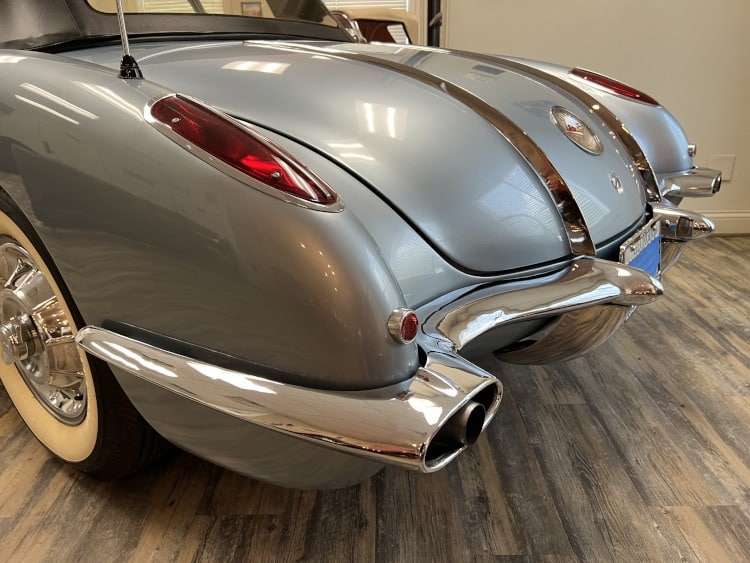 Close-up of the chrome tail section of a pristine 1958 Corvette, highlighting the distinctive quad taillights, dual exhaust pipes, and classic white wall tires.