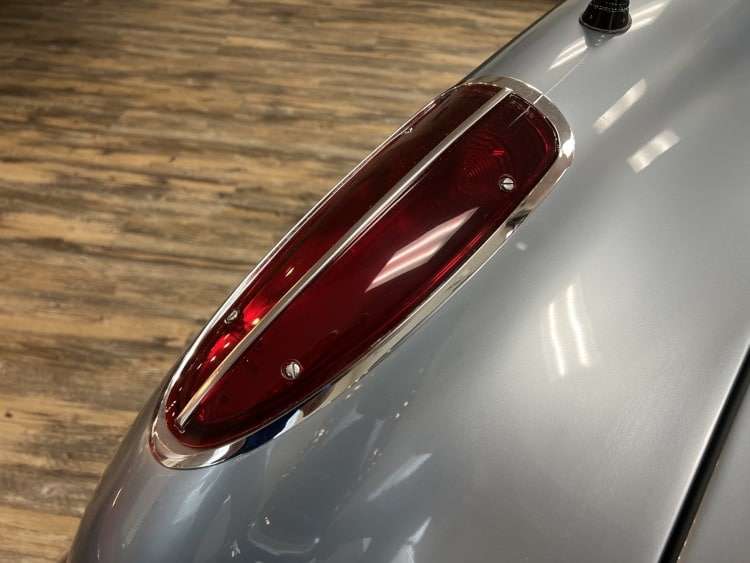 Close-up of the streamlined tail light on a silver 1958 Corvette, featuring a polished chrome bezel and a vibrant red lens.