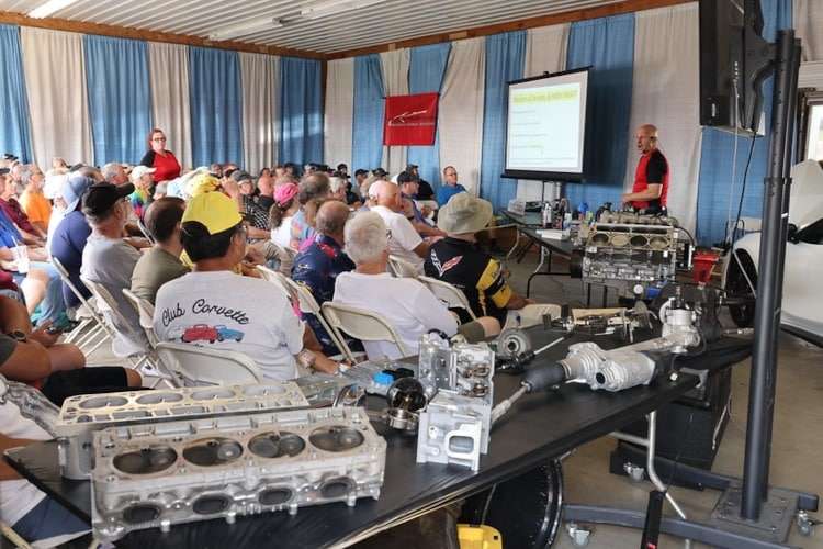 Photo showing a technical seminar at Corvettes at Carlisle 2025, where a speaker presents to a seated audience with a C8 Corvette engine and other parts on display."