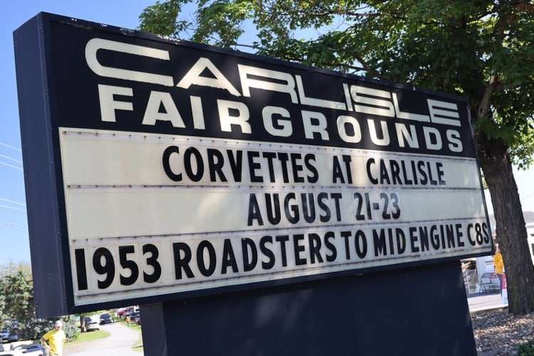 A large black sign for the Carlisle Fairgrounds announcing "Corvettes at Carlisle" from August 21-23, with the theme "1953 Roadsters to Mid-Engine C8s." Photo from Vettes of Atlanta Magazine/.