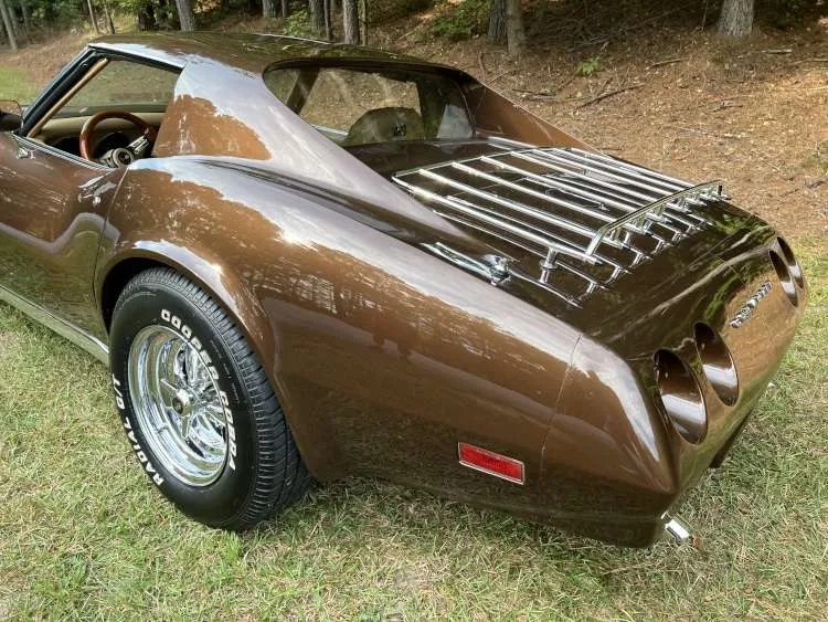 A rear-three-quarter view of the driver's side of a brown 1974 Corvette Stingray showing the rear deck luggage rack, iconic four taillights, and chrome wheels.