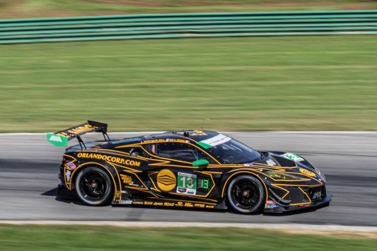 Side-profile of the #13 AWA Corvette Z06 GT3.R in its black and gold livery at speed on the race track.