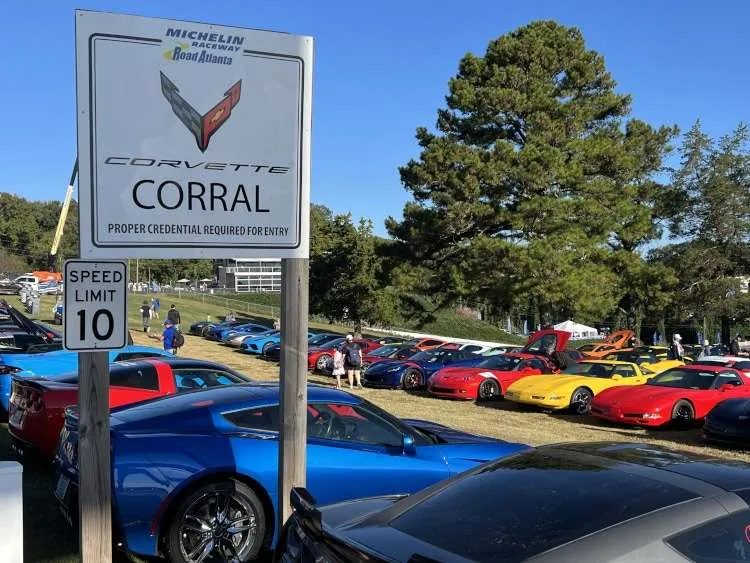 Sign for the official Corvette Corral at Michelin Raceway Road Atlanta with several generations of Corvettes (C8, C7, C6) parked on grass during Petit Le Mans 2025. (Credit: Vettes of Atlanta Magazine