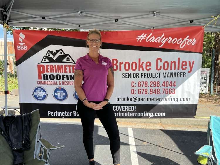 Brooke Conley, Senior Project Manager, stands smiling in front of a "Perimeter Roofing" banner, displaying her contact information and company awards under a white tent.