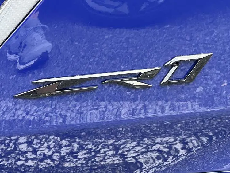 A Hysteria Purple 2025 Chevrolet Corvette ZR1 showing the functional split rear window, carbon fiber cooling vents, and the ZR1 name badge emblem on the rear decklid.