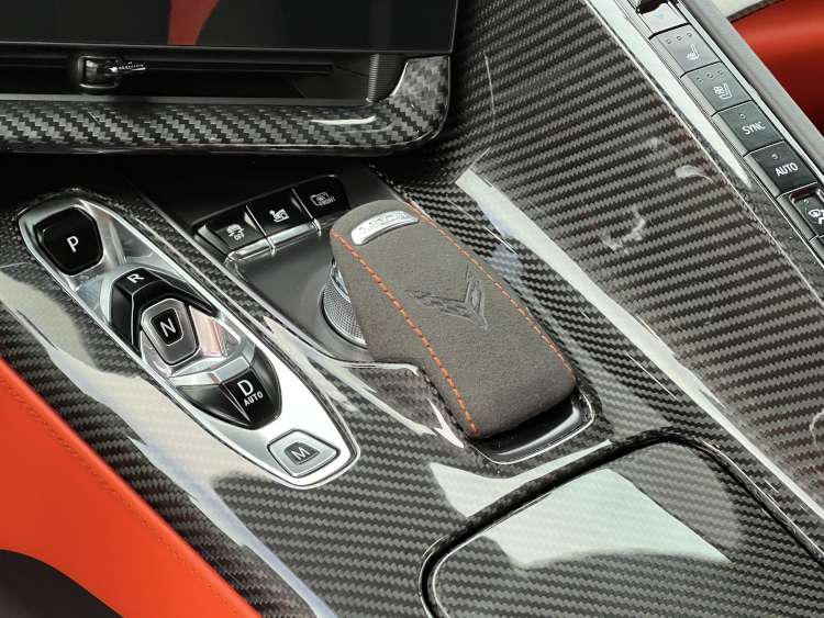 Close-up of the 2025 Corvette ZR1 interior featuring a high-gloss carbon fiber center console, a microsuede-wrapped gear selector with orange stitching, and Habanero orange leather trim.