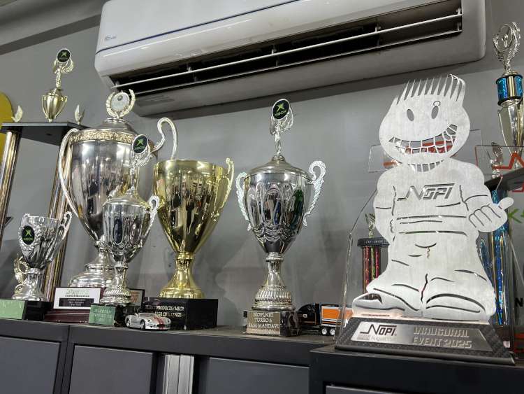 A collection of silver and gold automotive racing trophies on display at Mahdavi Motorsports, including the NOPI Inaugural Event 2025 award and NDRA Championship trophies.