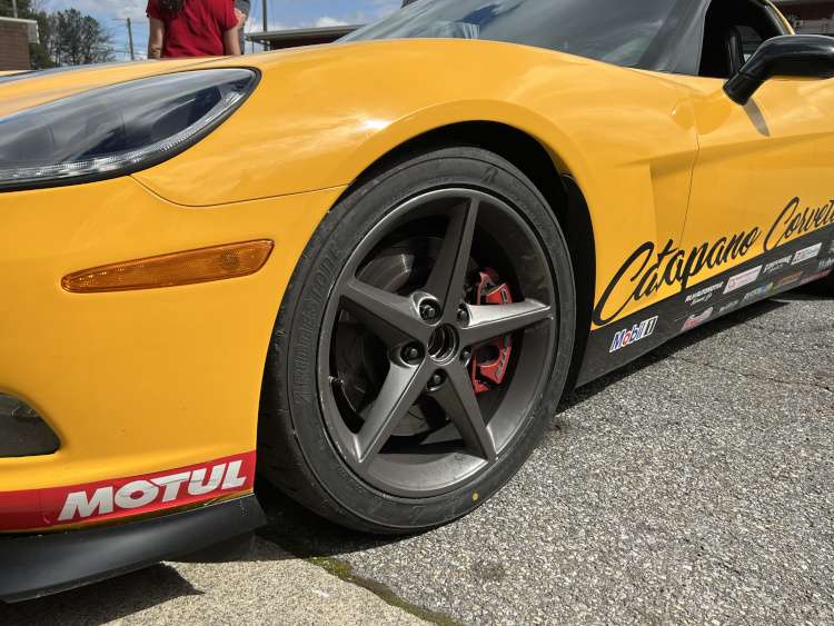 Low-angle front quarter view of a yellow Chevrolet Corvette C6 featuring charcoal five-spoke wheels, Bridgestone Potenza tires, red Corvette brake calipers, and a Motul sponsor decal on the front splitter.