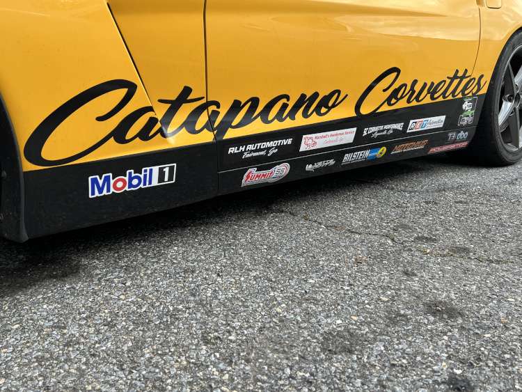 Low-angle view of the yellow door on a Chevrolet Corvette C6 track car, featuring a large "Catapano Corvettes" decal and multiple sponsor stickers including Mobil 1, Summit Racing, and Bilstein.
