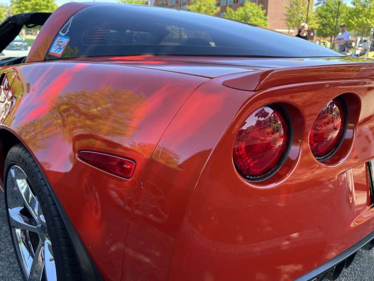 Rear driver’s side view of a metallic deep orange Chevrolet Corvette C6, showing aftermarket black multi-spoke wheels, massive carbon fiber rear fender flares, and an aggressive rear diffuser with four exhaust tips.