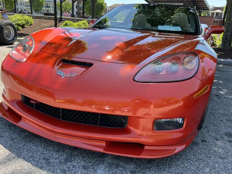 Rear quarter panel and taillight of a modified black high-performance sports car, likely a Chevrolet Corvette C7, parked indoors at an auto event or show in Atlanta. The image features visible modifications like a wide-body kit, carbon fiber accents, and a custom alloy wheel, set against a background with people and a 'STREET GRIND' banner.