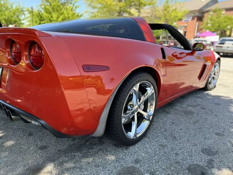 Rear quarter panel and taillight of a black high-performance sports car, likely a Chevrolet Corvette, parked at an indoor car show in Atlanta.