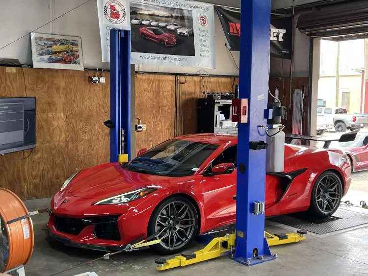 Red Chevrolet Corvette C8 Z06 strapped to a chassis dynamometer for performance tuning in a professional shop with Corvette club banners in the background.