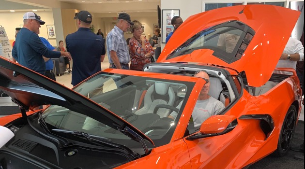 Diverse age crowd looking at Sebring Orange C8 Corvette