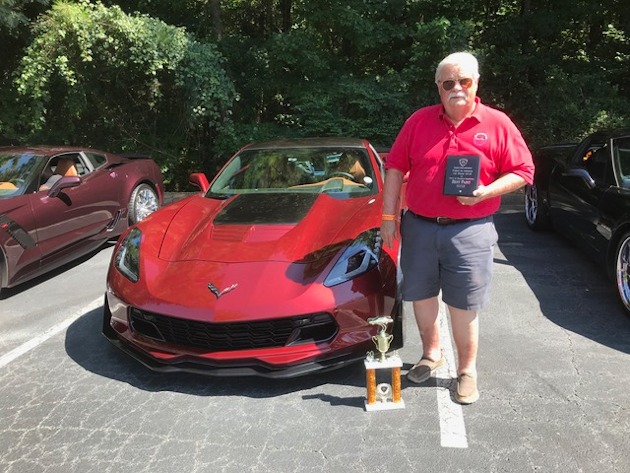 A man holding a car show trophy infront of a C7 Corvette