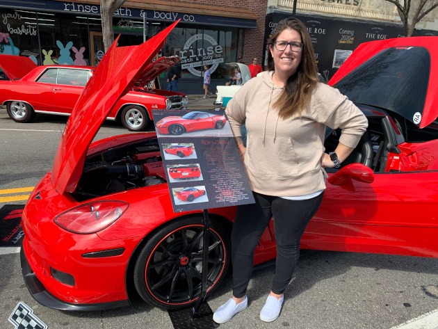 Katie Falanga posing beside a red Corvette and her Open Road Design car show board