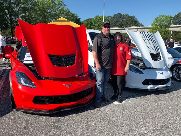 Owners of a red Z06 and a white Grand Sport Corvettes standing beside their cars