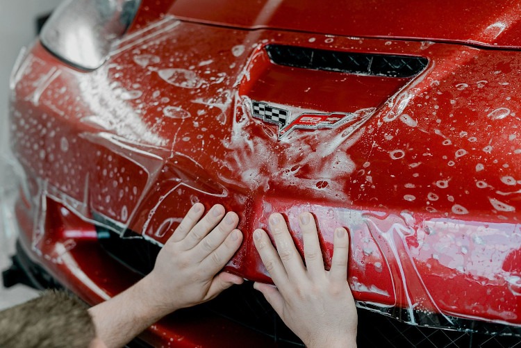 XPEL paint protection film being adjusted on a red Corvette