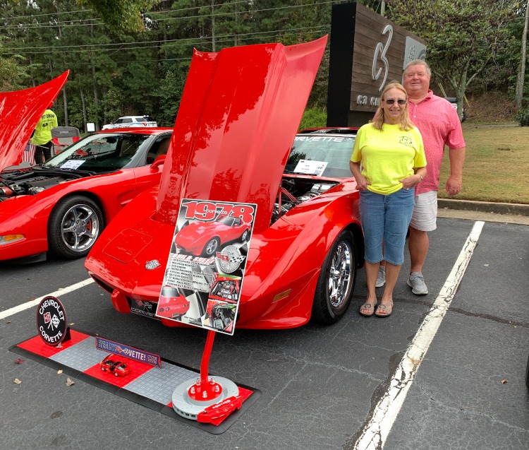 Twop people standing in front of a custom C3 red Corvette coupe