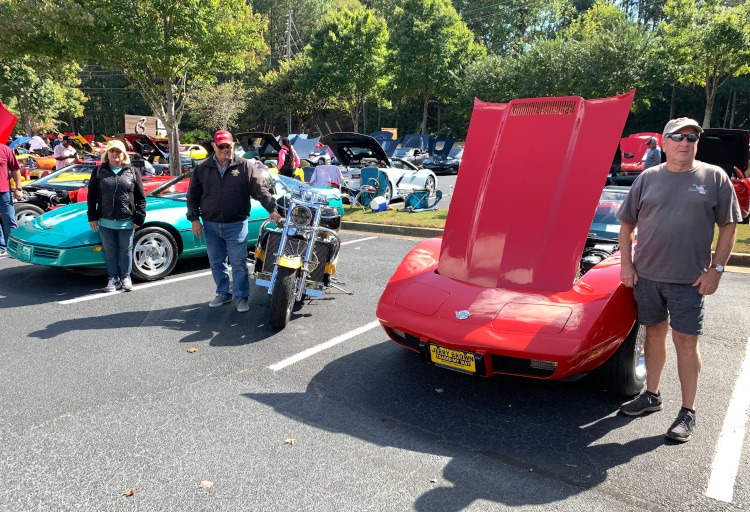 Three people standing at a Corvette car show