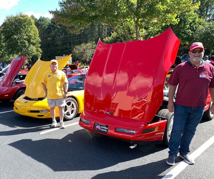 Two men standing beside their Corvettes at a car show