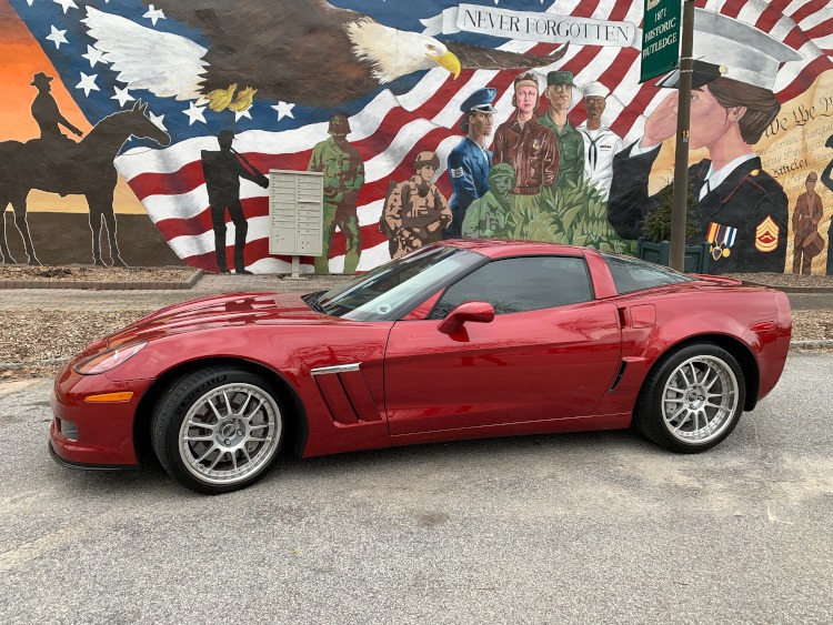 Crystal Red Corvette parked in front of a patriotic mural