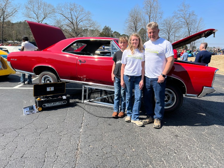 People standing beside a red Pontiac GTO on a lift