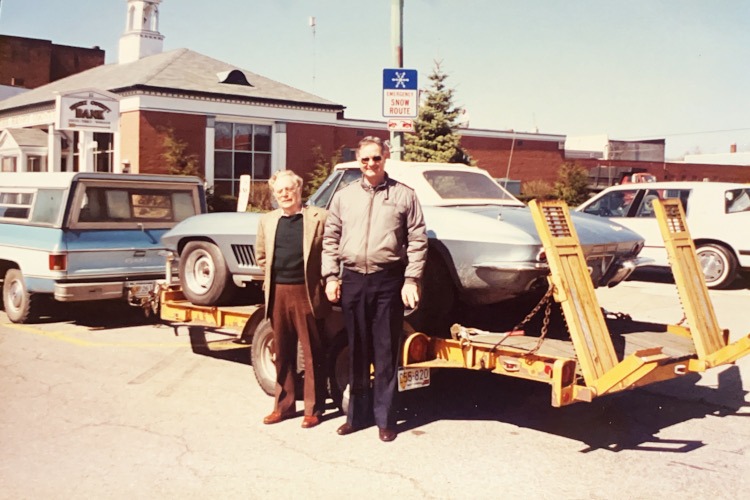 Two men standing beside a 1967 blue Corvette on a trailer