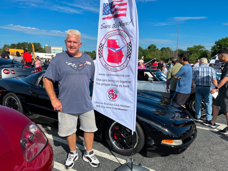 Man standing by a Classic Glass Corvette Club banner