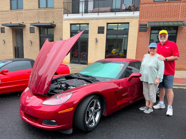 Two people standing beside a crystal red C6 Corvette