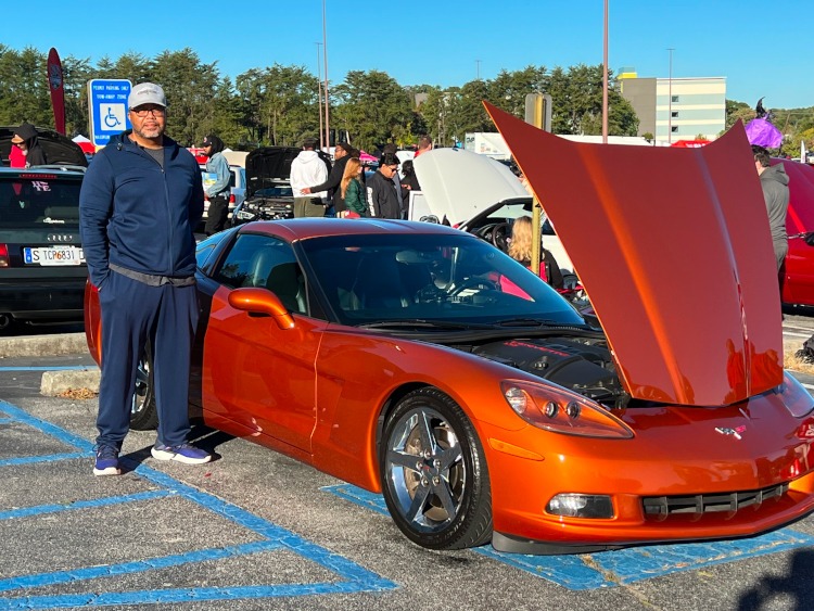 Man Standing beside a sixth-generation Corvette coupe.