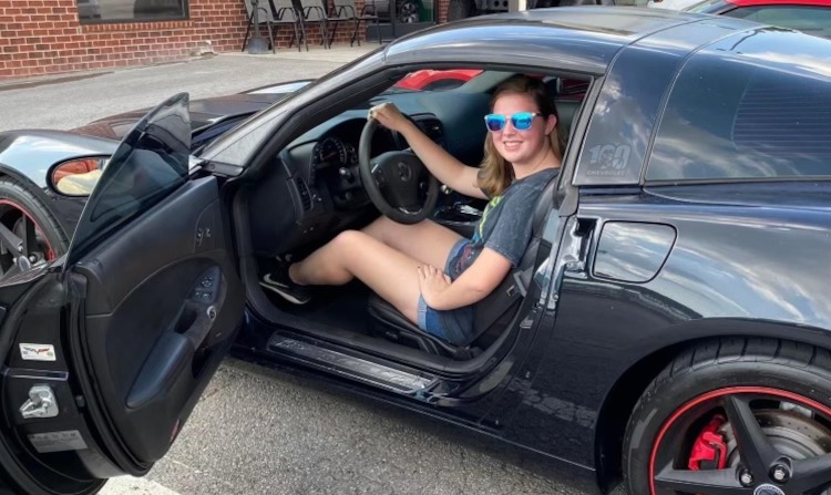 Young girl sitting in a black Corvette coupe