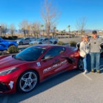A couple standing beside a red C8 Corvette
