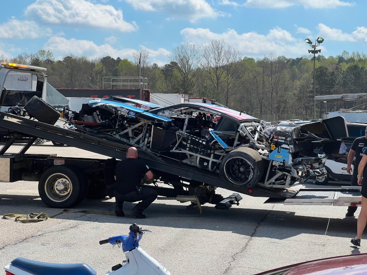 Wrecked race car on a flatbed wrecker at a race track