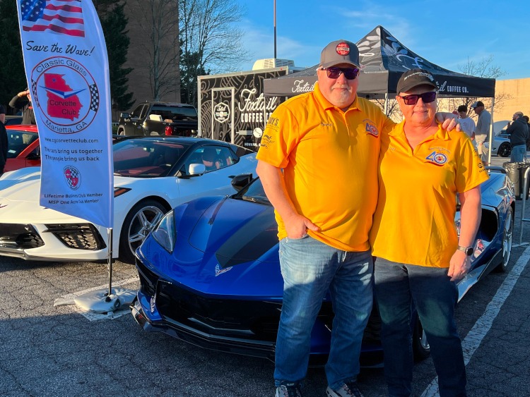 Two people are standing before a 2023 Elkhart Lake Blue Corvette convertible.