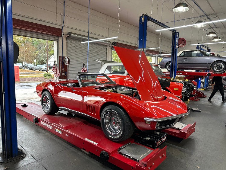 A red convertible Corvette on a repair shop lift.