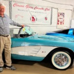 A man standing beside a teal C1 era Corvette convertible.