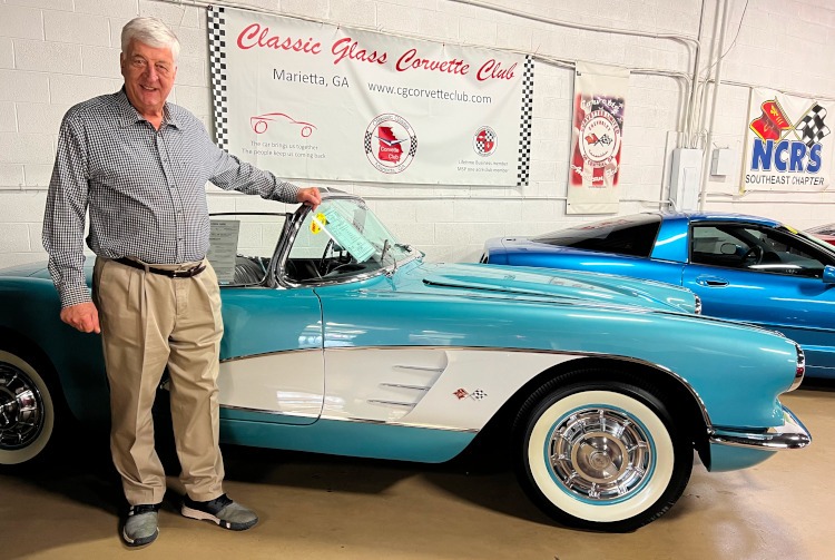 A man standing beside a teal C1 era Corvette convertible.