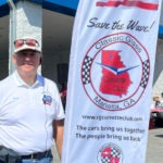 A man standing beside a Classic Glass Corvette club banner
